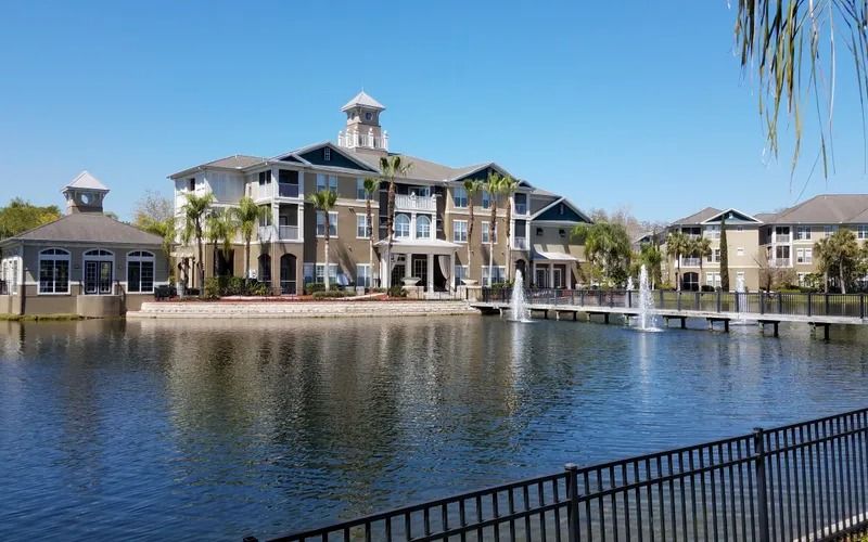 Apartment complex beside a lake with fountains and a bridge. Blue sky and sunny day.